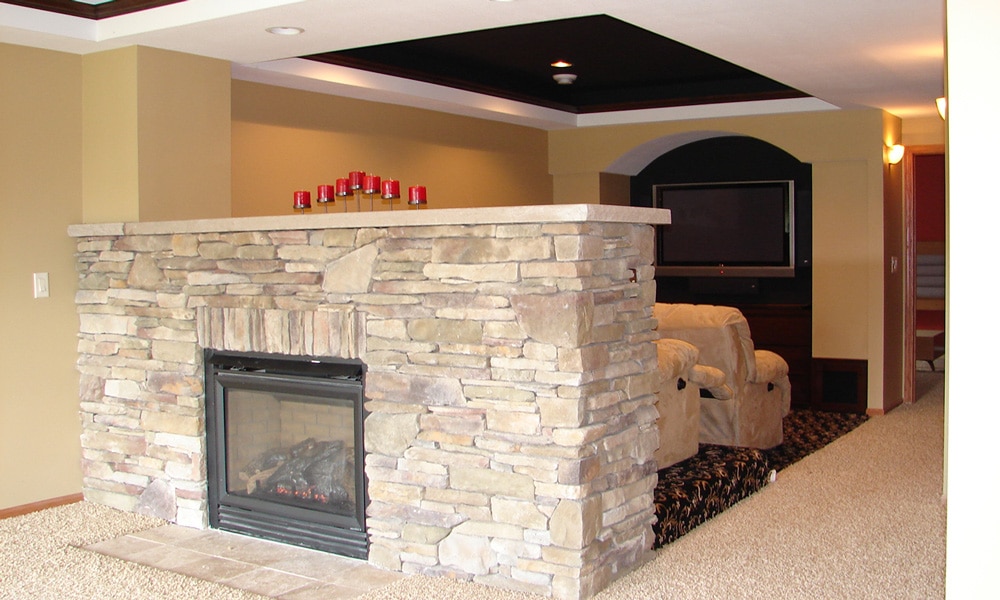 Lower level basement remodeling project completed by Titus Contracting includes movie theater area with large screen and recliner chairs and a stone surround fireplace.