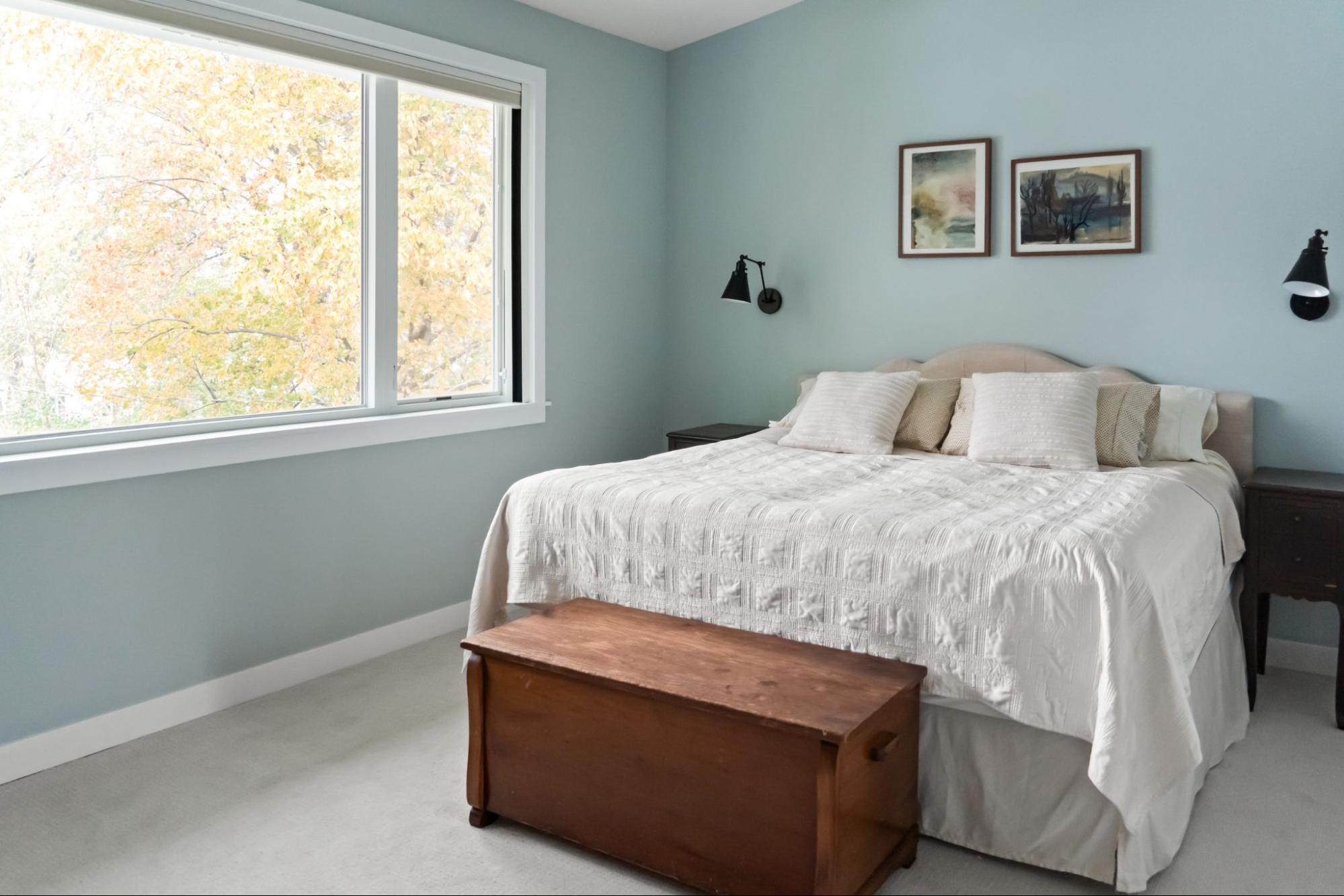 a bedroom with blue walls and a large double bed, flanked by modern sconces